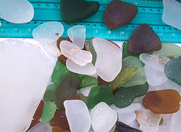 four different shades of green sea glass with ruler